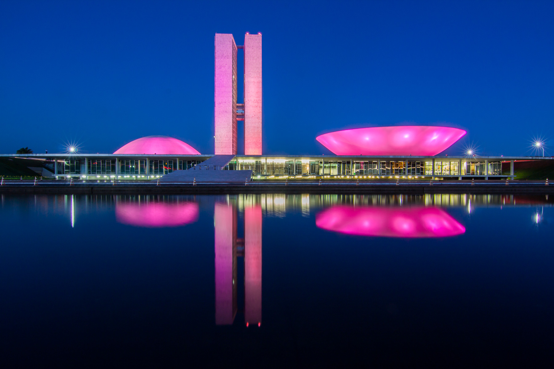Éclairées en rose, une grande tour et deux immenses coupoles se reflètent dans l’eau de nuit.