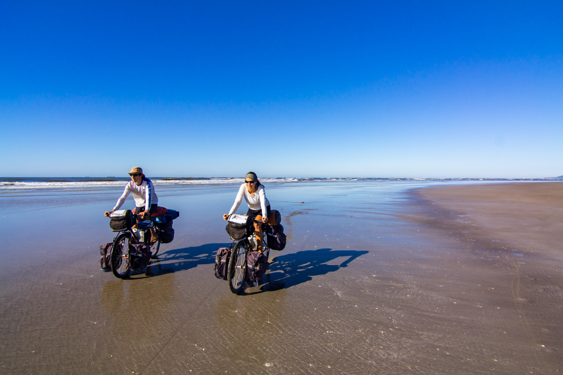 Deux cyclotouristes roulent vers la caméra sur le sable au bord de l’océan.