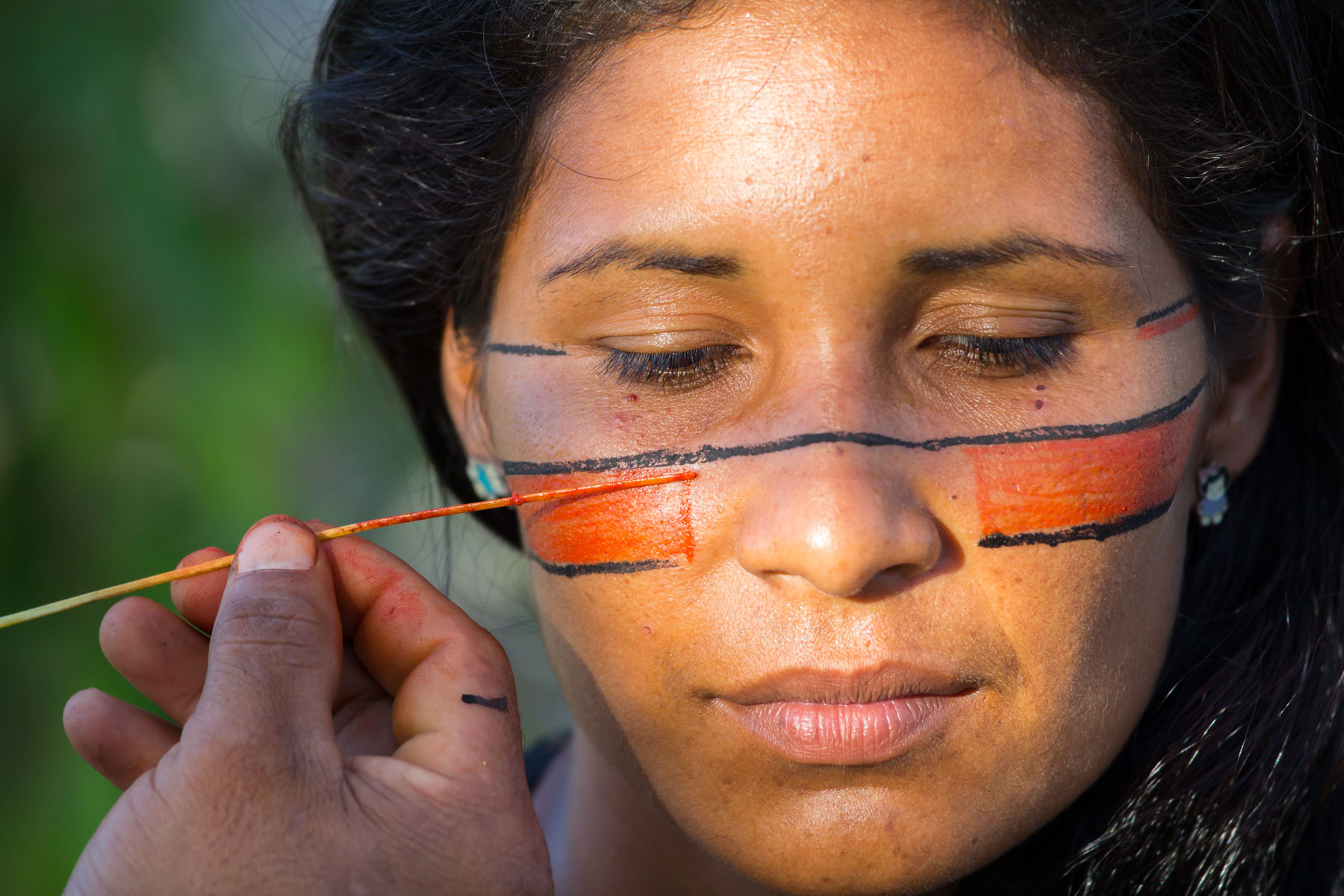 Portrait d’une femme de la tribu Pataxós au Brésil avec des peintures traditionnelles rouge et noir sur le visage.