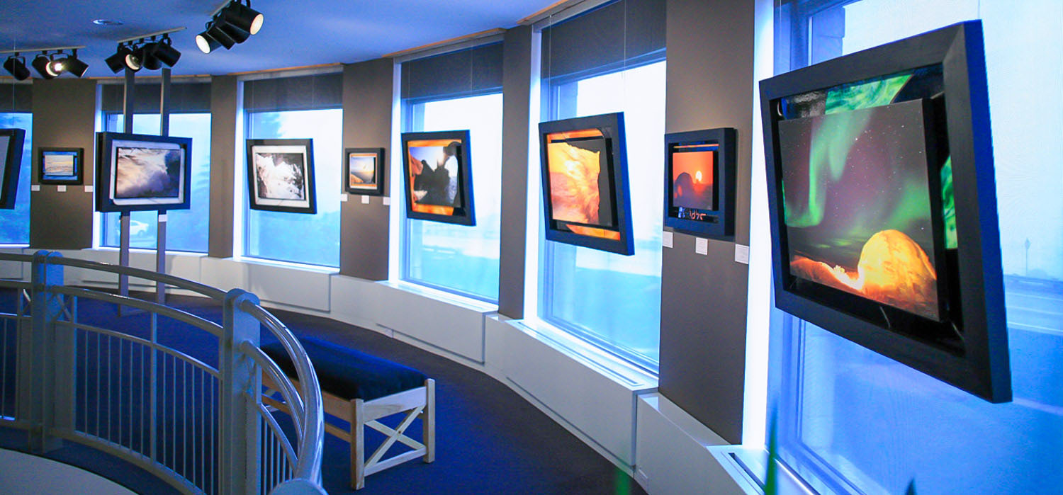 Oeuvres artistiques exposées dans une salle d’exposition avec de grandes fenêtres. Au premier plan, une œuvre représentant un igloo avec une aurore boréale verte.