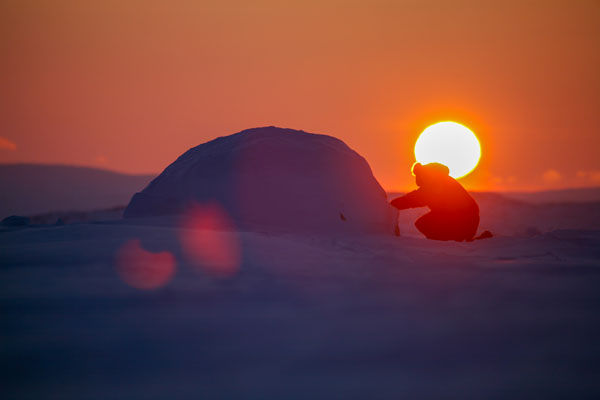 Coucher du soleil avec la silhouette d’une personne et d’un igloo sur la banquise au Nunavut (Canada).