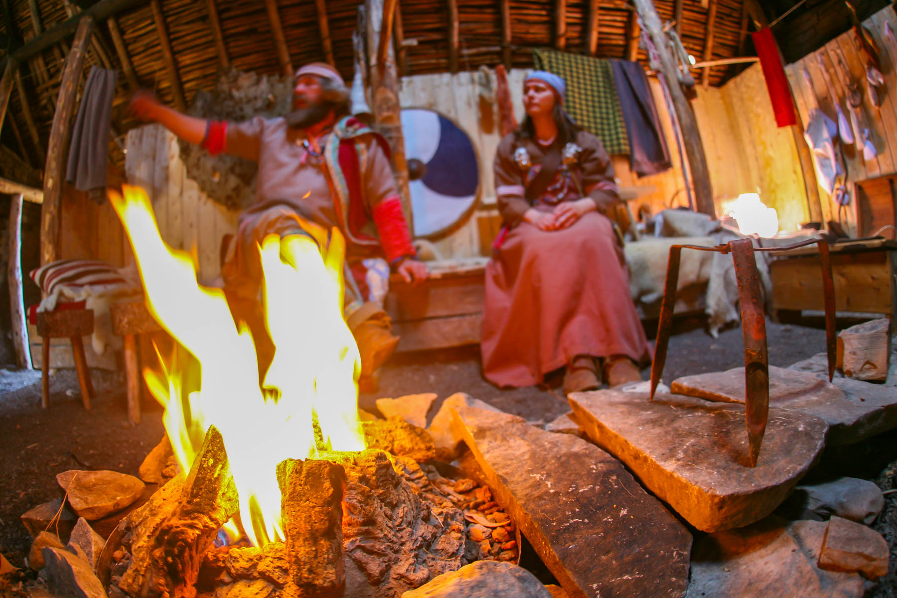 Un feu à l’intérieur d’une maison traditionnelle viking avec un homme et une femme vêtue en costume d’époque.
