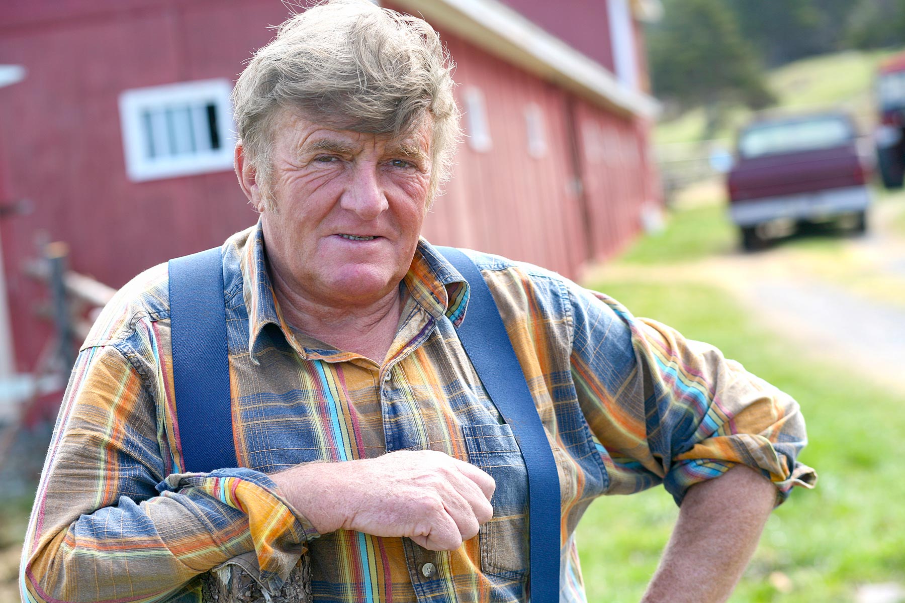 Portrait d’un homme dans la soixantaine près de sa ferme peinte en rouge.