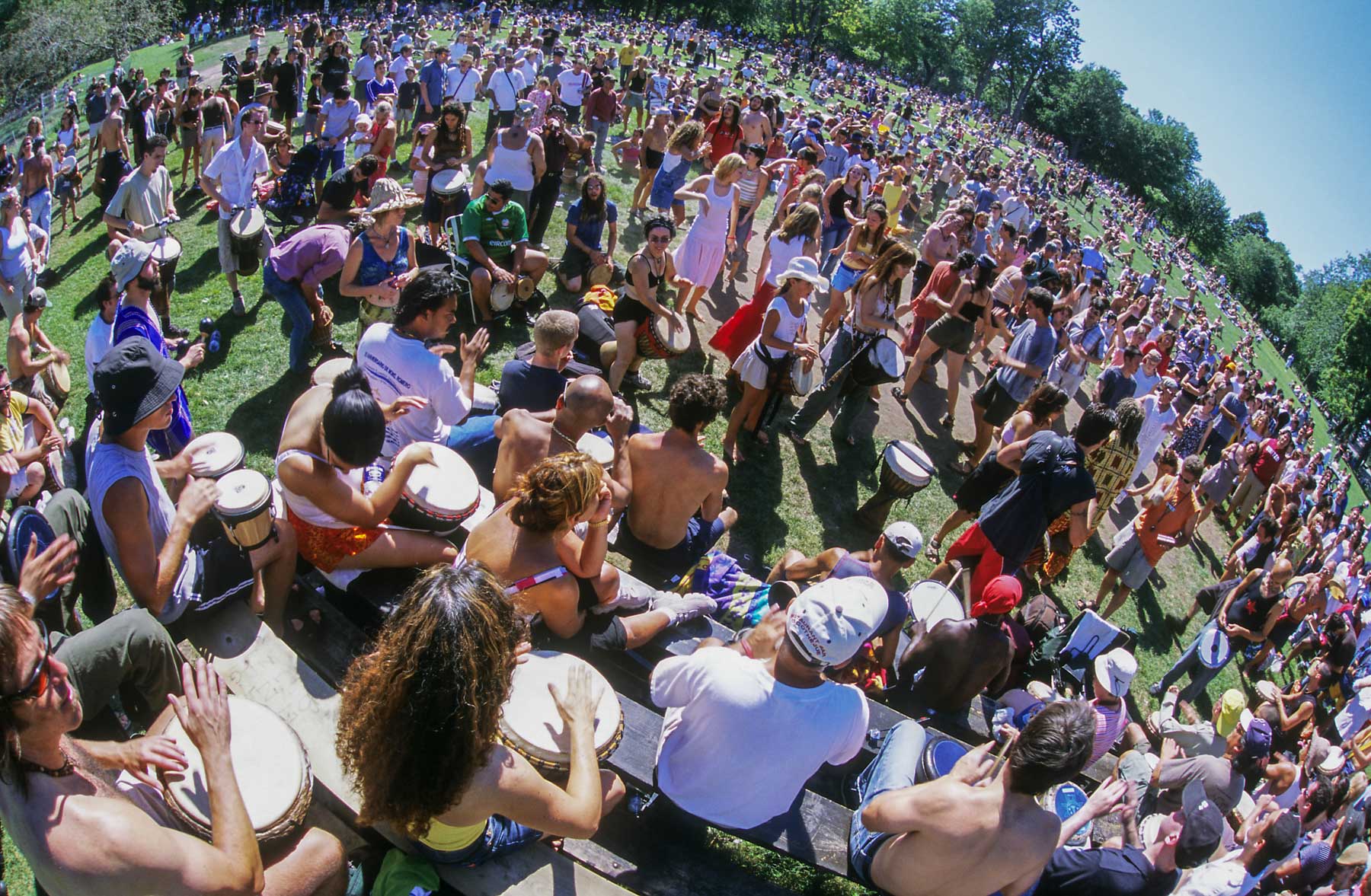 Rassemblement de plusieurs centaines de personnes jouant du tam-tam dans un parc verdoyant.
