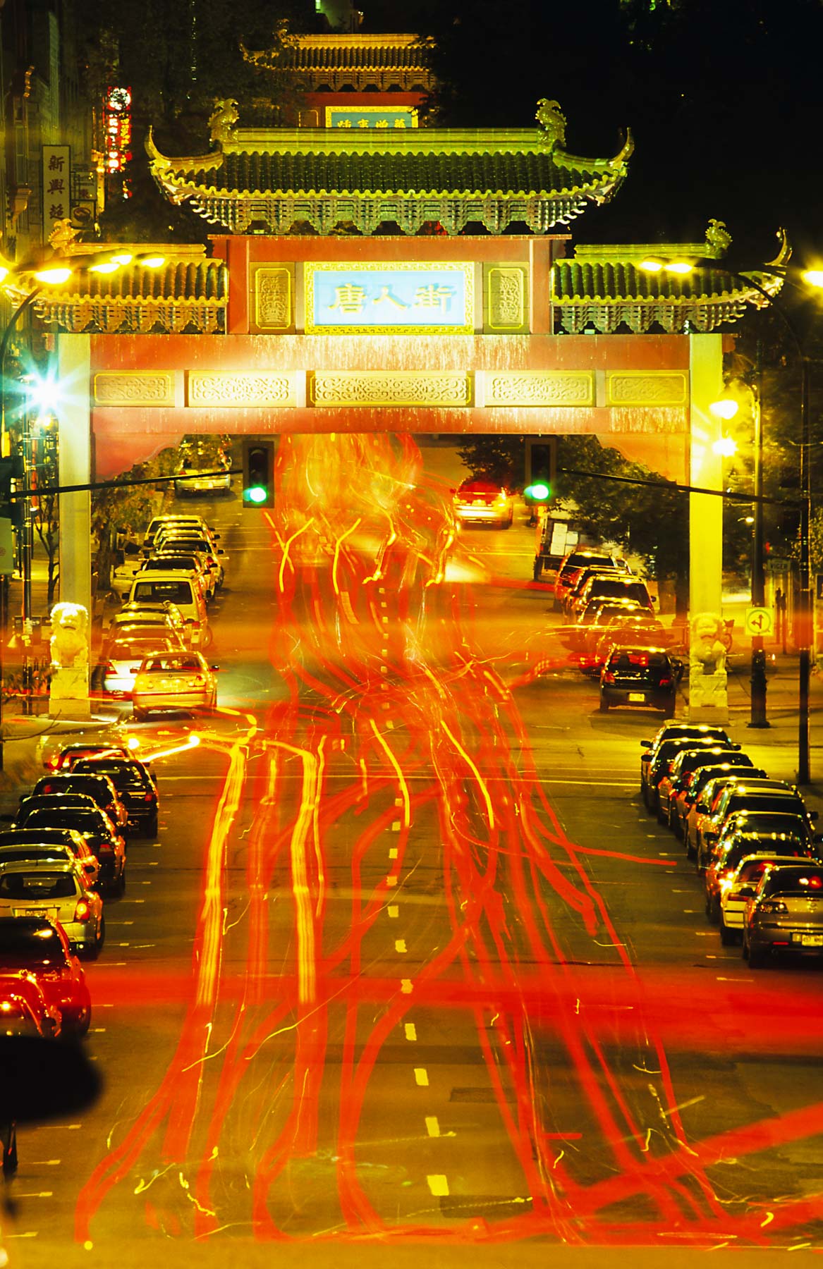 Lumières des voitures circulant de nuit sous une haute arche à l’entrée du quartier chinois.