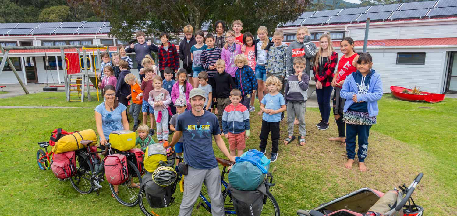 Les élèves d’une petite école néo-zélandaise posent sur une estrade avec une famille du Canada voyageant à vélo.
