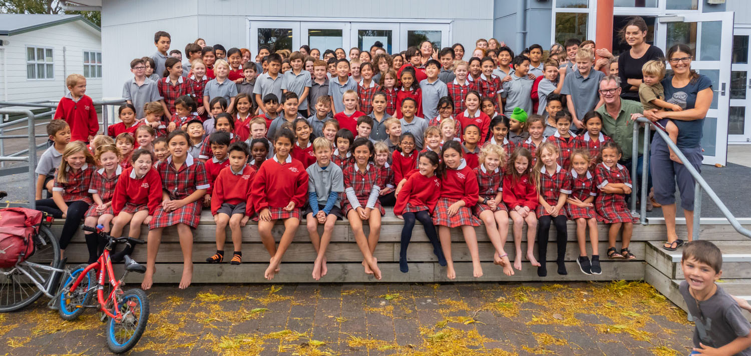 Les élèves d’une petite école néo-zélandaise posent dans le terrain de jeux avec une famille du Canada voyageant à vélo.