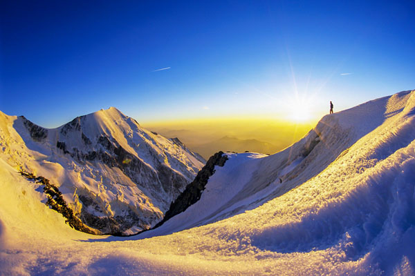 Petite silhouette d’une personne dans un paysage grandiose de montagnes, de neiges et de glaciers au coucher de soleil.