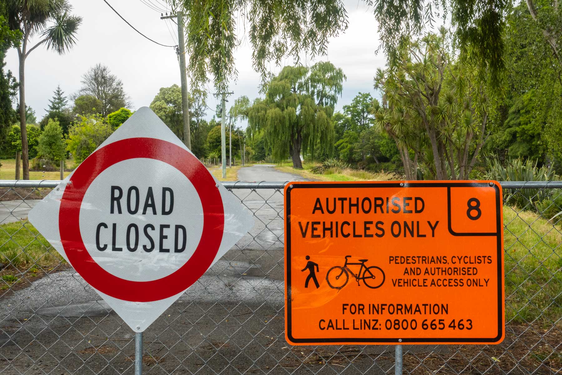 Sur une barrière grillagée, un panneau rouge et blanc indique que la route est fermée. Une pancarte orange précise aussi que les piétons, les vélos et les personnes autorisées peuvent circuler.
