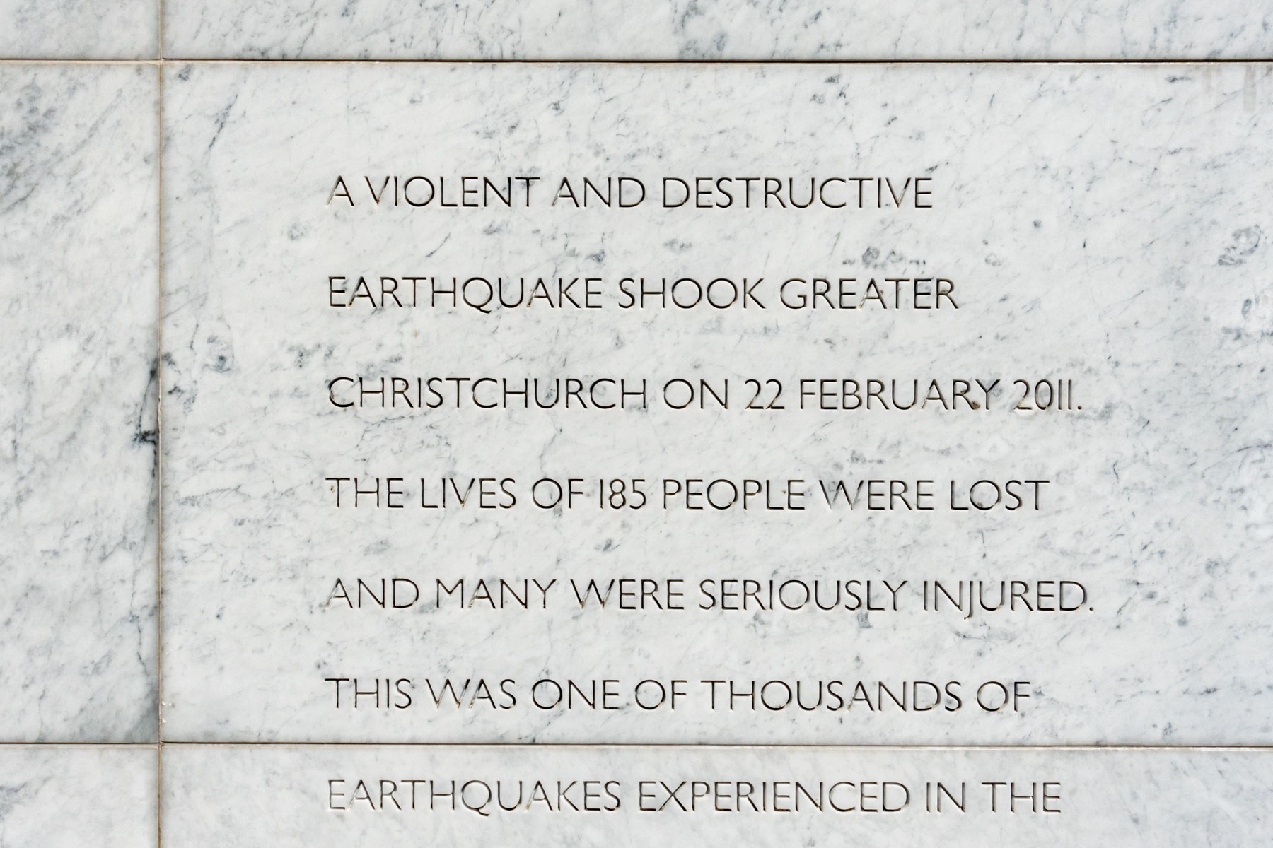 Sculpté dans le marbre, un texte en anglais explique qu’un violent tremblement de terre à dévasté la ville de Christchurch, faisant 185 morts et de nombreux blessés.
