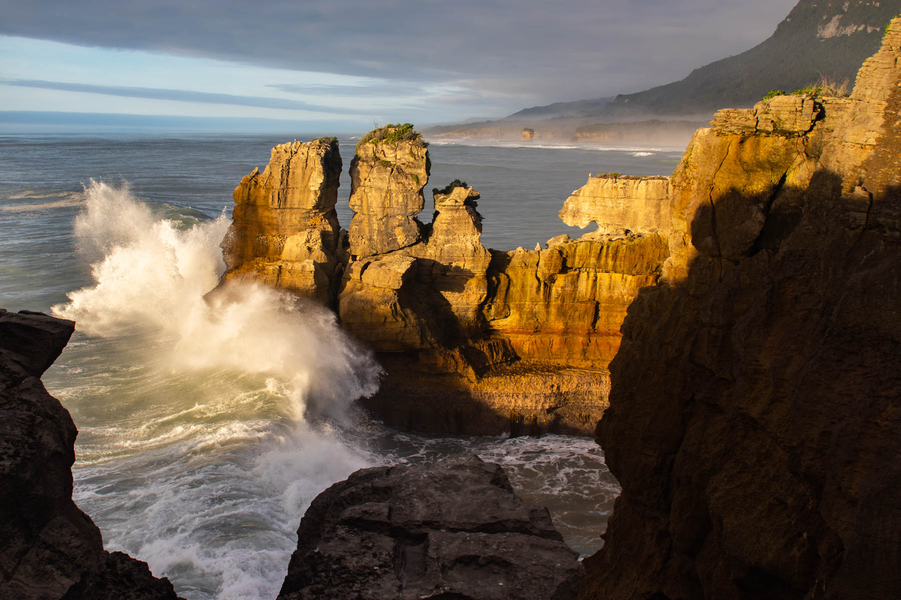 Au coucher du soleil, une immense vague se brise contre une falaise.