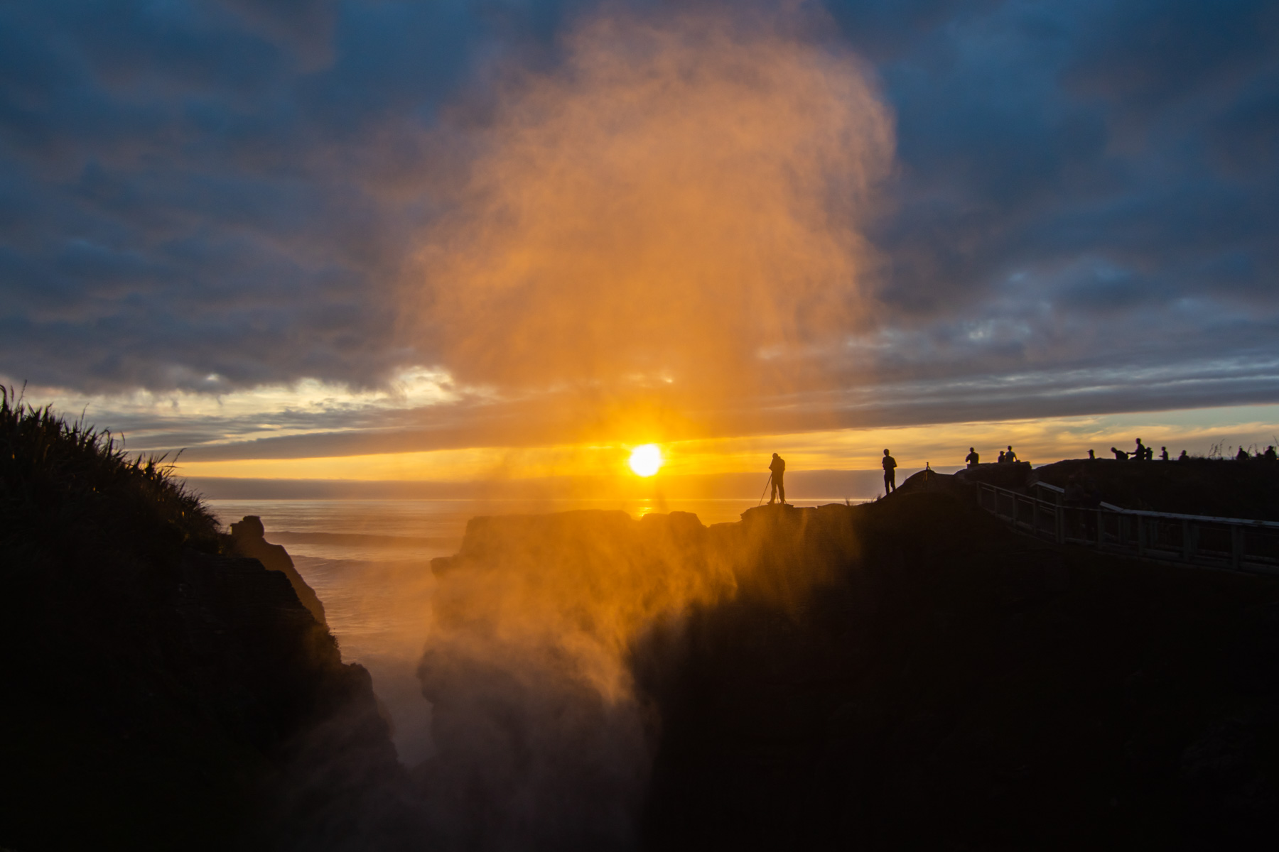 Silhouettes de personnes debout au coucher du soleil alors qu’un jet d’eau jaillit dans les airs.