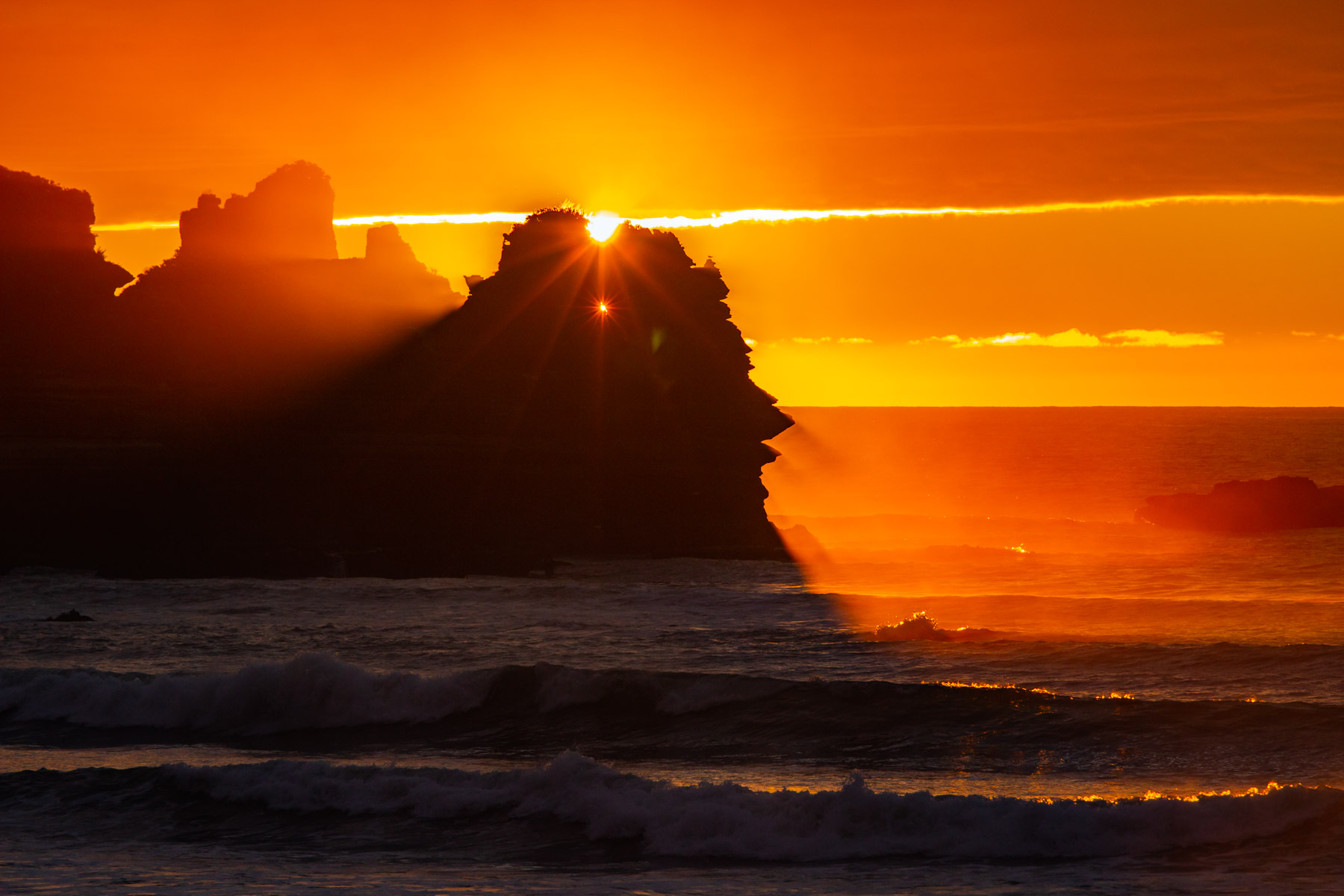 En fin de journée, les rayons du soleil pénètrent dans les trous d’une falaise située au bord d’une mer agitée.