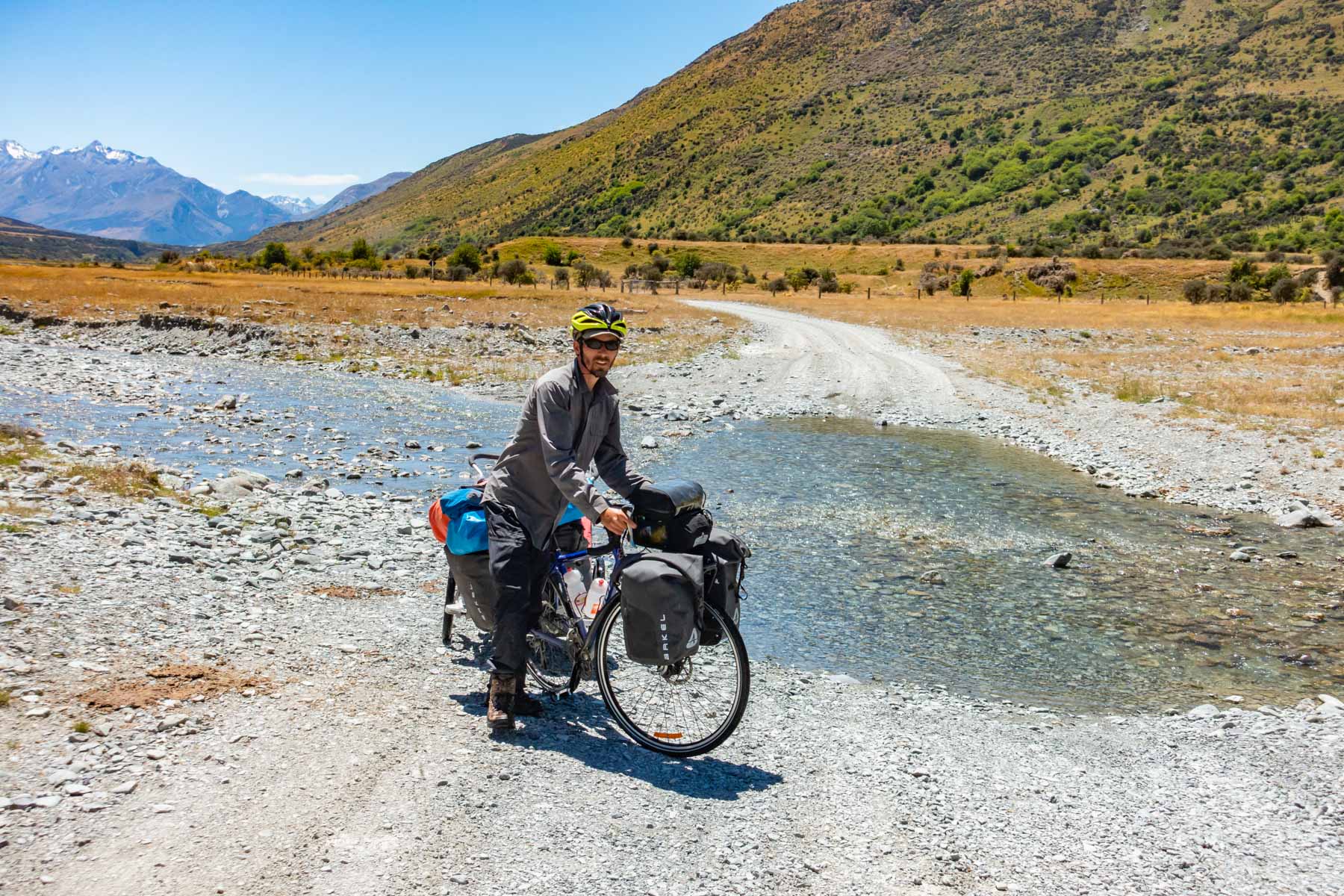 En suivant un chemin de gravier, un homme traverse un petit ruisseau avec son vélo de cyclotourisme.
