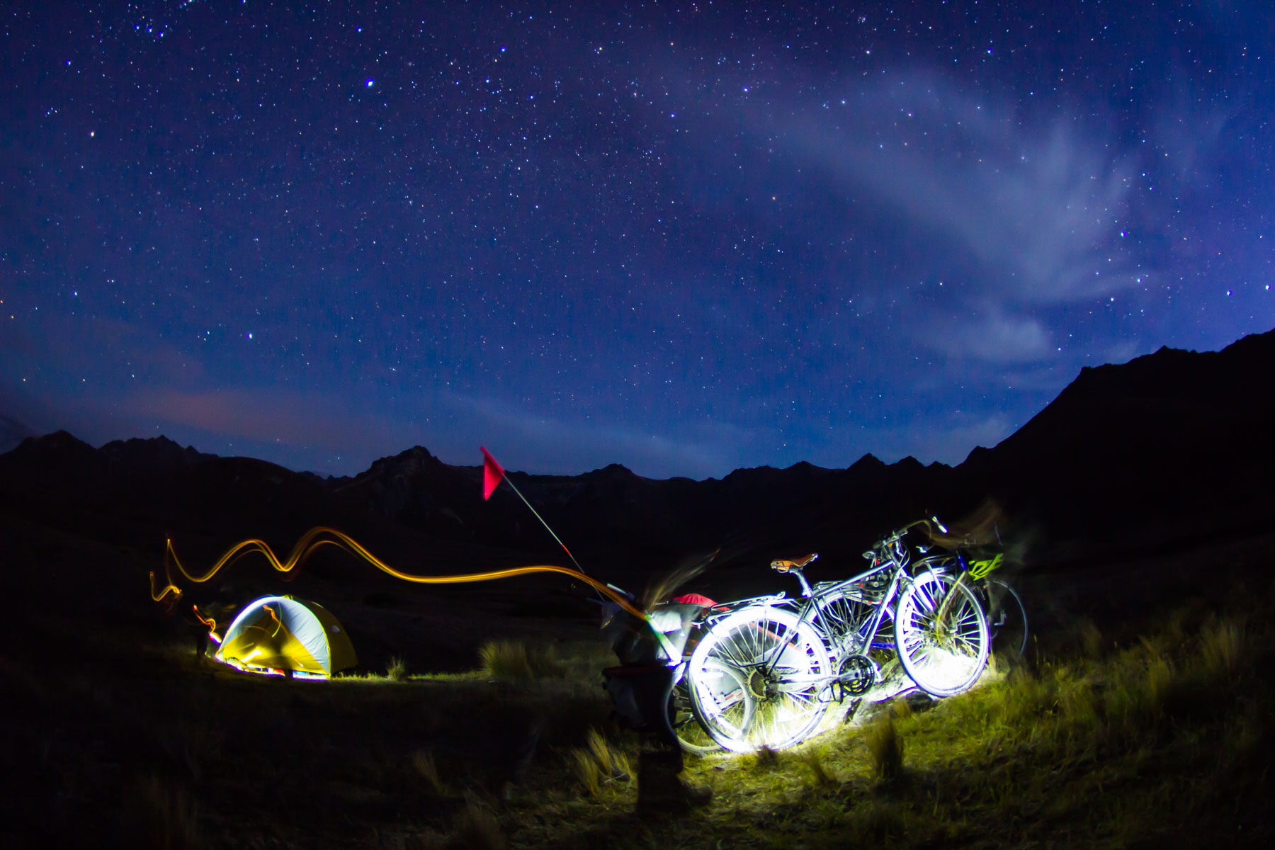 Une lampe éclaire et se déplace sur deux vélos et une tente sous un ciel étoilé.