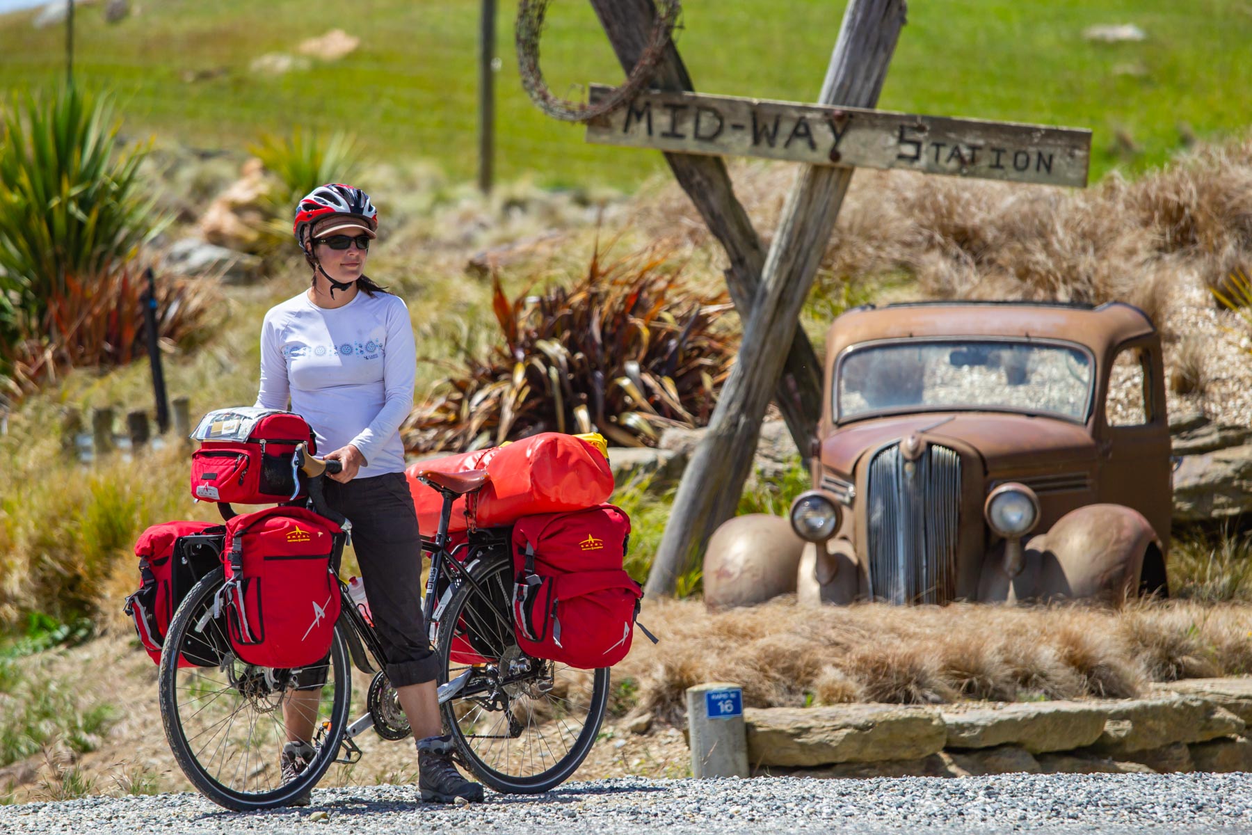 Une femme pose avec son vélo de cyclotourisme devant une vieille voiture rouillée à Mid-Way.