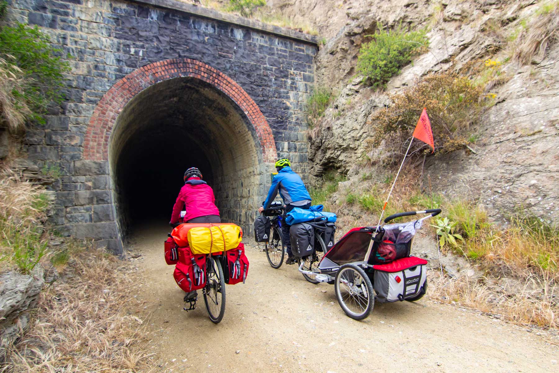 Sur une piste de gravier, deux cyclistes entrent dans un tunnel avec leurs vélos chargés.