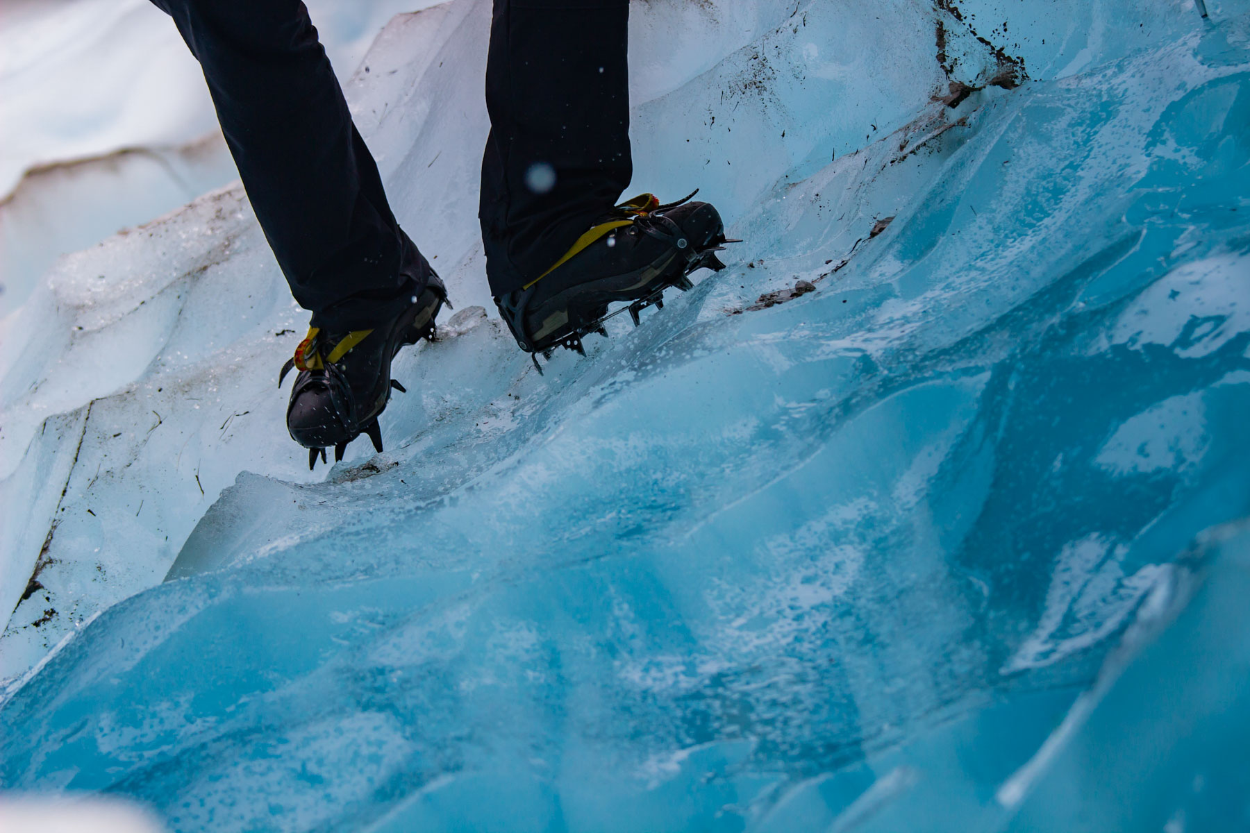 Une personne marche avec des crampons sur une glace bleutée.