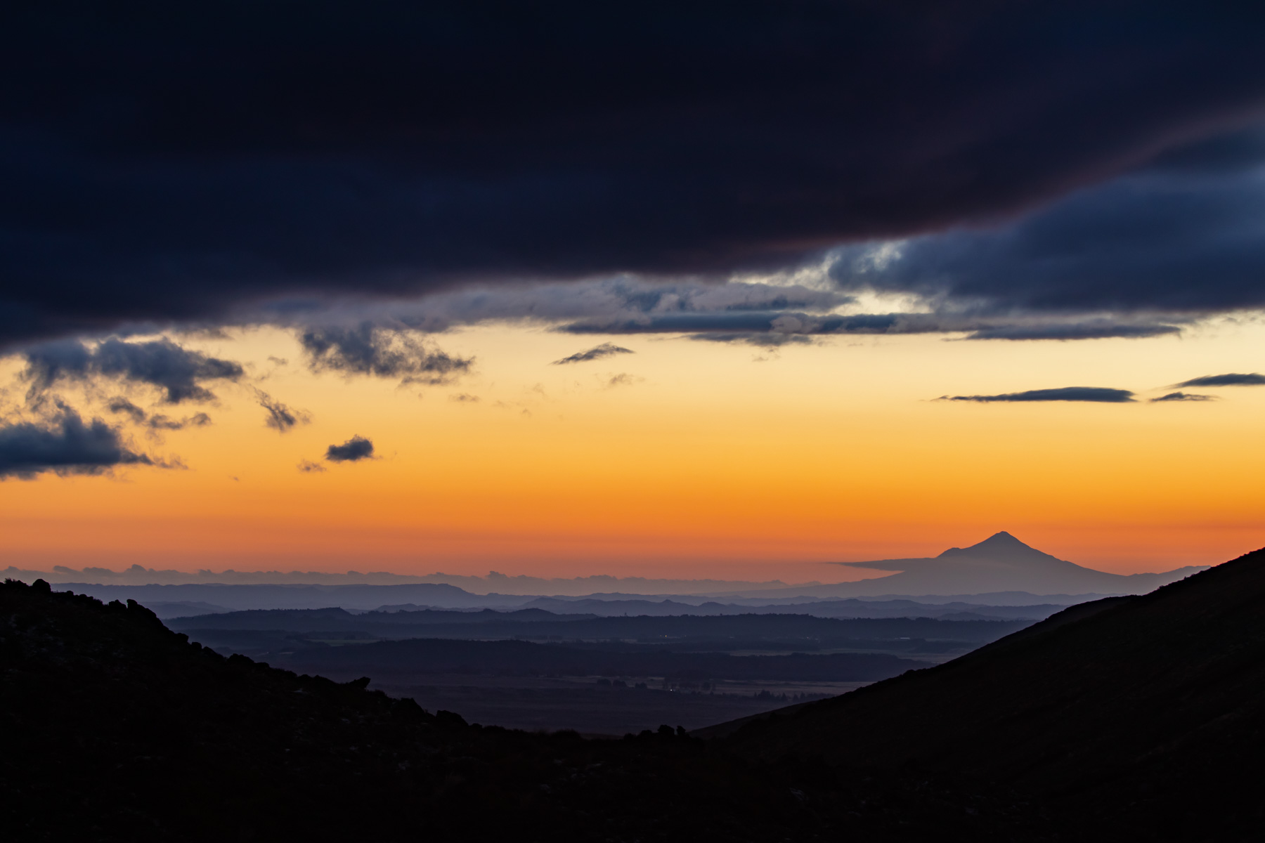 La silhouette du volcan Taranaki se dessine à l’horizon au coucher de soleil.