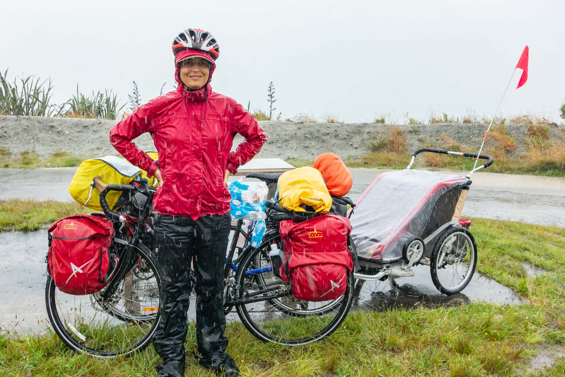 In the pouring rain, a woman poses for a photo with her loaded bicycle.