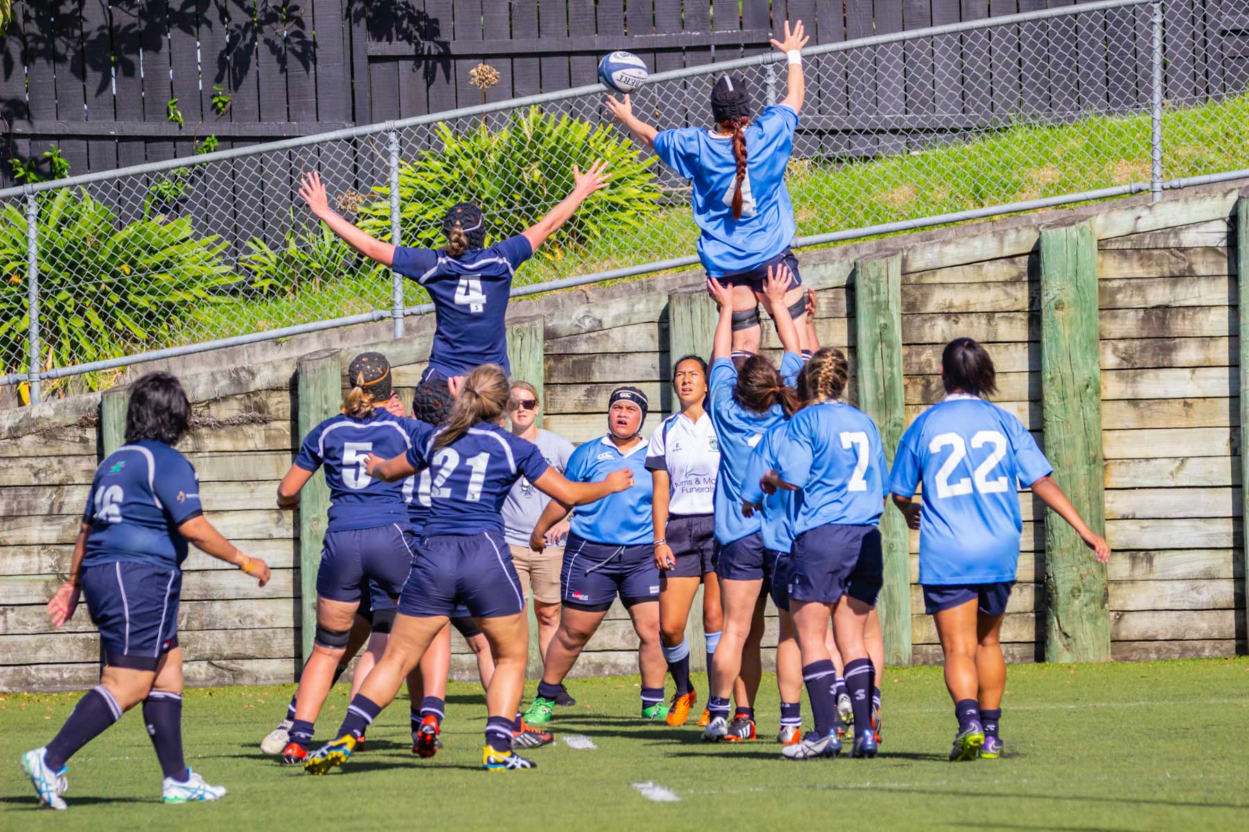 Durant un match, les deux équipes féminines de rugby tentent d’attraper le ballon lancé dans les airs.