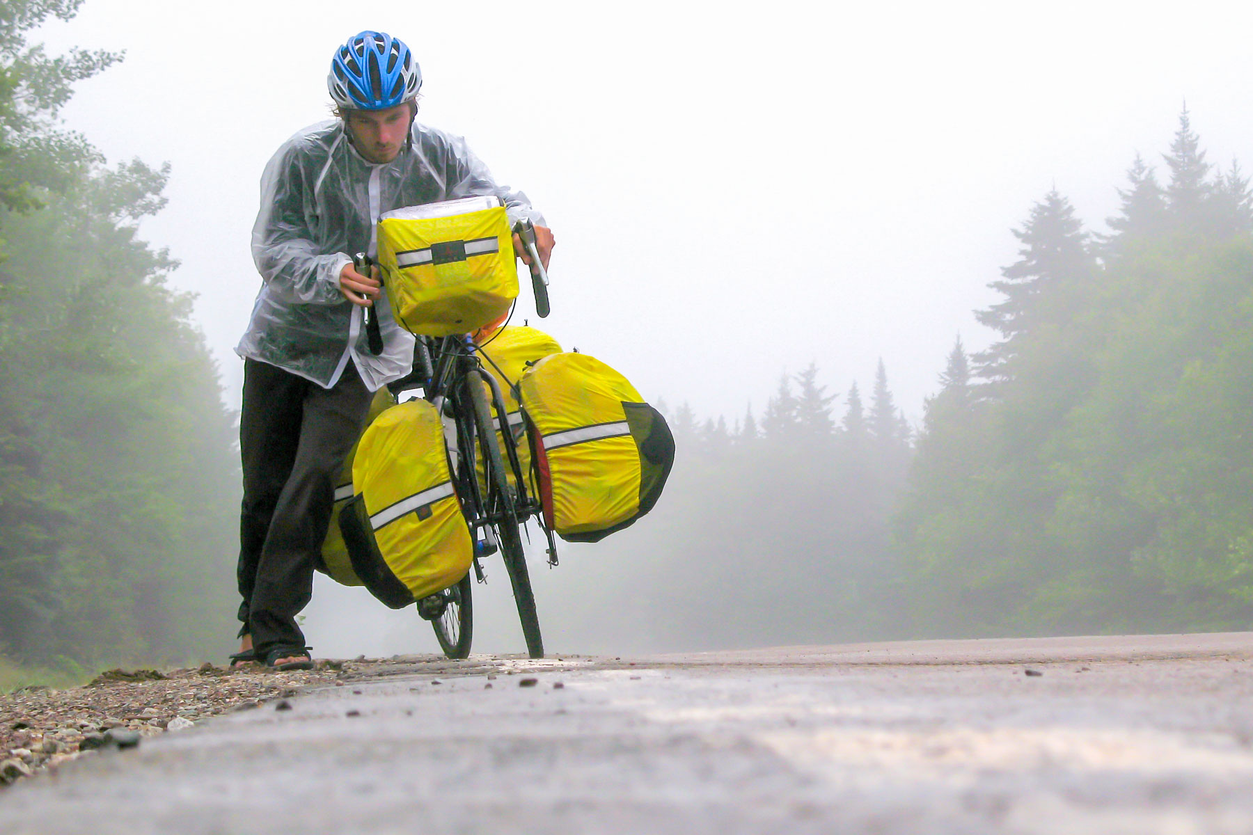 Par une journée brumeuse, un homme pousse son vélo de cyclotourisme chargé dans une montée abrupte.